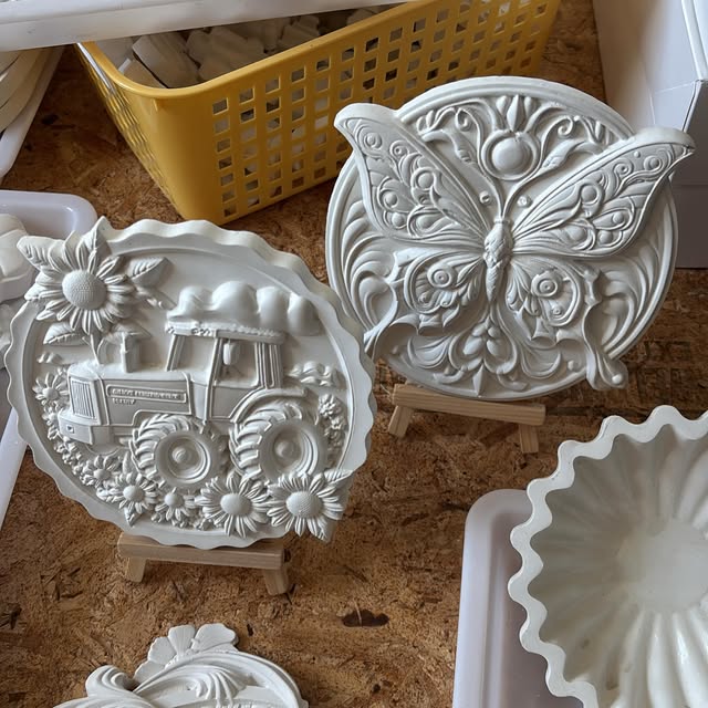 Round plaster plaques with a butterfly, a tractor with sunflowers, and a sunflower, standing on small wooden easels.