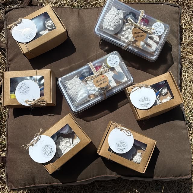 Small kraft gift boxes with windows and clear boxes tied with twine, each holding a plaster piece and a round tag.
