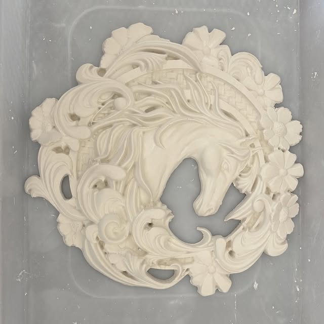 A round plaster medallion of a horse's head framed in flowers and swirls.
